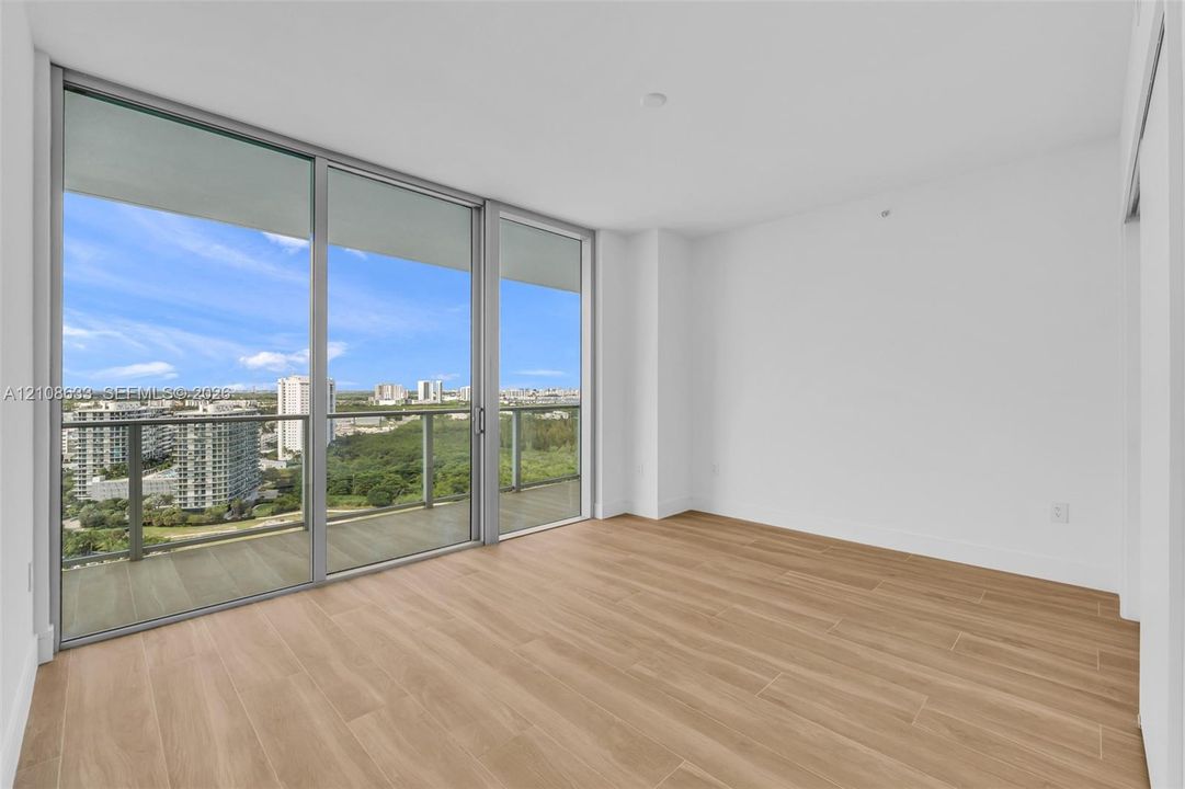 Floor-to-ceiling glass sliding doors, private balcony with metal railing, wood-finish flooring, and expansive exterior landscape