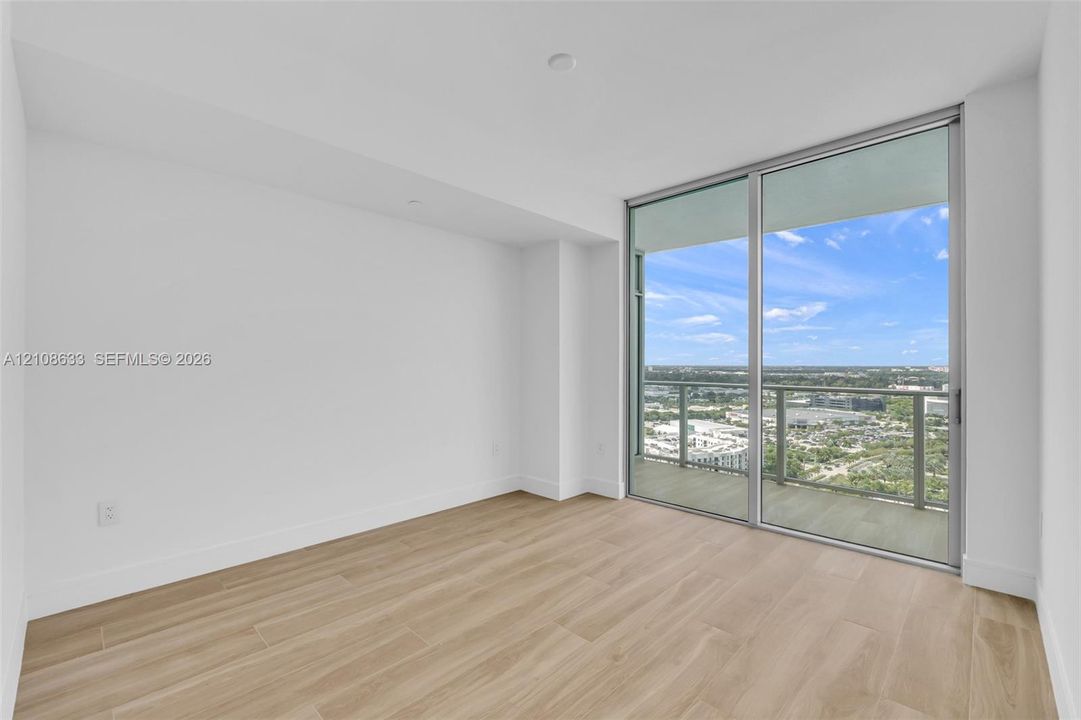 Floor-to-ceiling sliding glass doors, wood-finish flooring, and a private balcony with metal railing