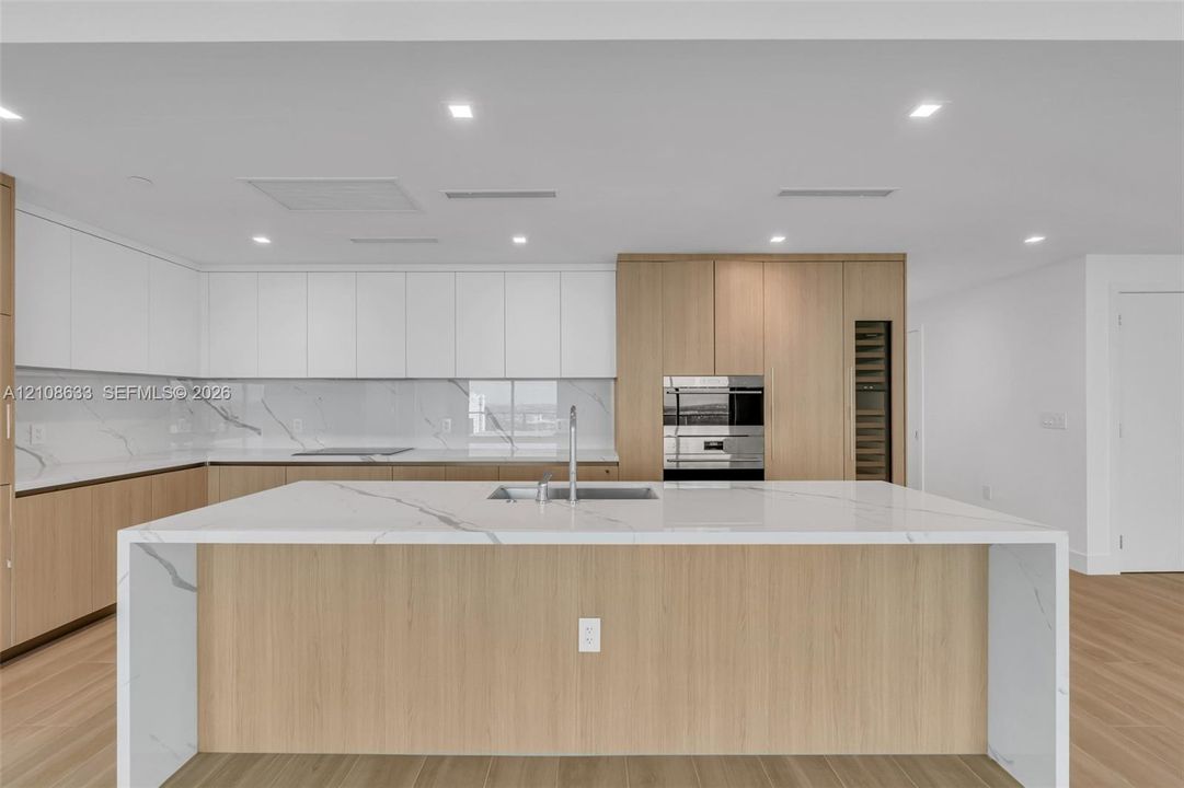 Modern kitchen featuring a waterfall-edge island with stone-finish countertops, two-tone cabinetry, recessed ceiling lighting, a built-in oven, and wood-finish flooring