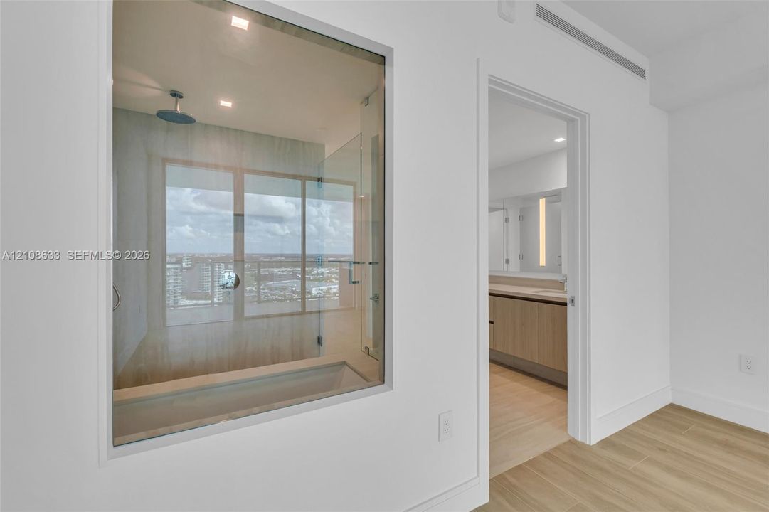 Interior space featuring wood-finish flooring, a glass-enclosed soaking tub with a ceiling-mounted rainfall showerhead, and dual-vanity cabinetry with integrated lighting