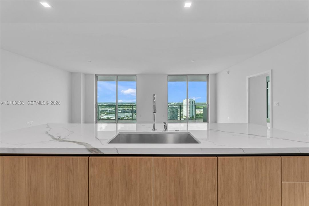 Kitchen island with waterfall-edge stone countertop, undermount stainless steel rectangular sink, tall arching faucet, wood-finish cabinetry, and floor-to-ceiling glass sliding doors
