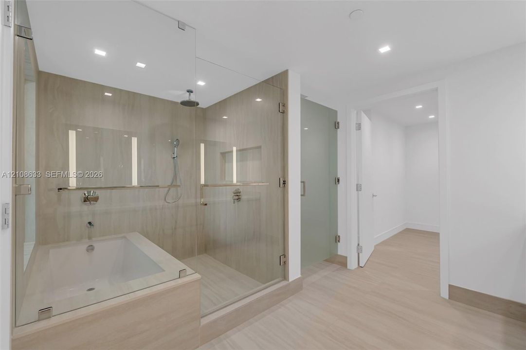 Glass-enclosed wet room featuring a deep soaking tub, walk-in shower with stone-tile surround, integrated recessed shelving, and wood-finish flooring