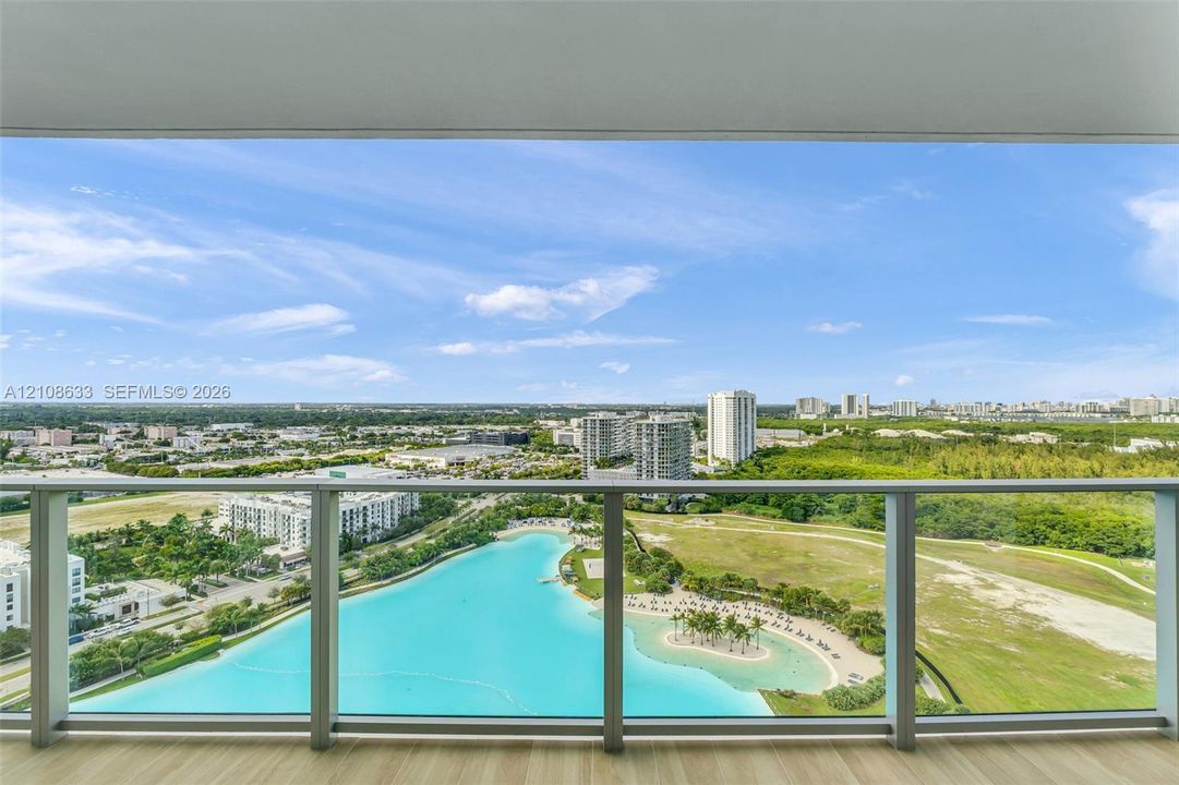 Full-height glass balcony enclosure with metal framing, wood-finish flooring, and expansive panoramic scenery including a central lagoon