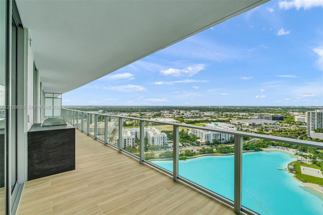Covered balcony featuring wood-finish tile flooring, a built-in outdoor grill station with stone-finish cladding, and a glass panel railing