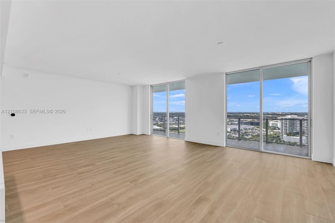 Open-concept living space featuring wood-finish flooring, floor-to-ceiling glass sliding doors, and exterior balcony access