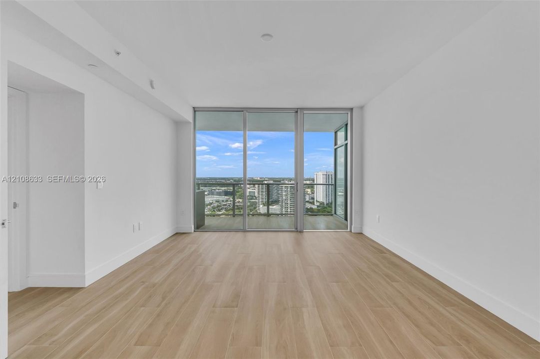 Open-concept interior featuring wood-finish flooring, floor-to-ceiling glass sliding doors, and a private balcony with an urban skyline horizon