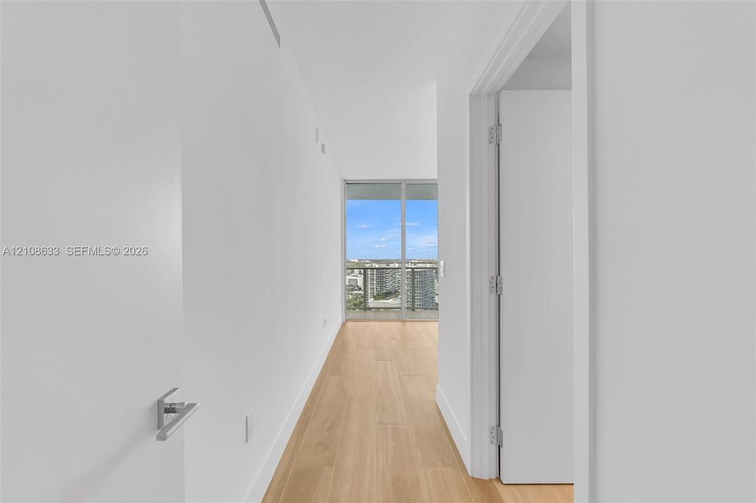 Hallway featuring wood-finish flooring, crisp white walls, and floor-to-ceiling glass paneling with an exterior railing