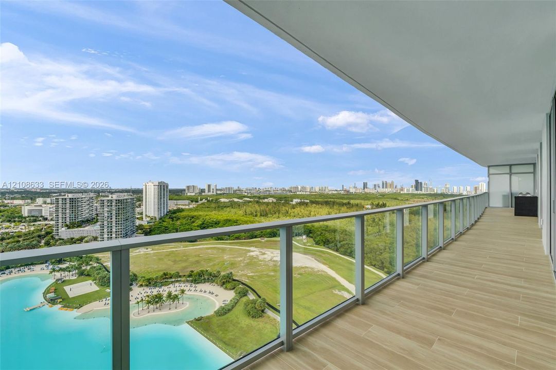 Expansive covered balcony featuring wood-finish tile flooring and a full-length glass panel railing