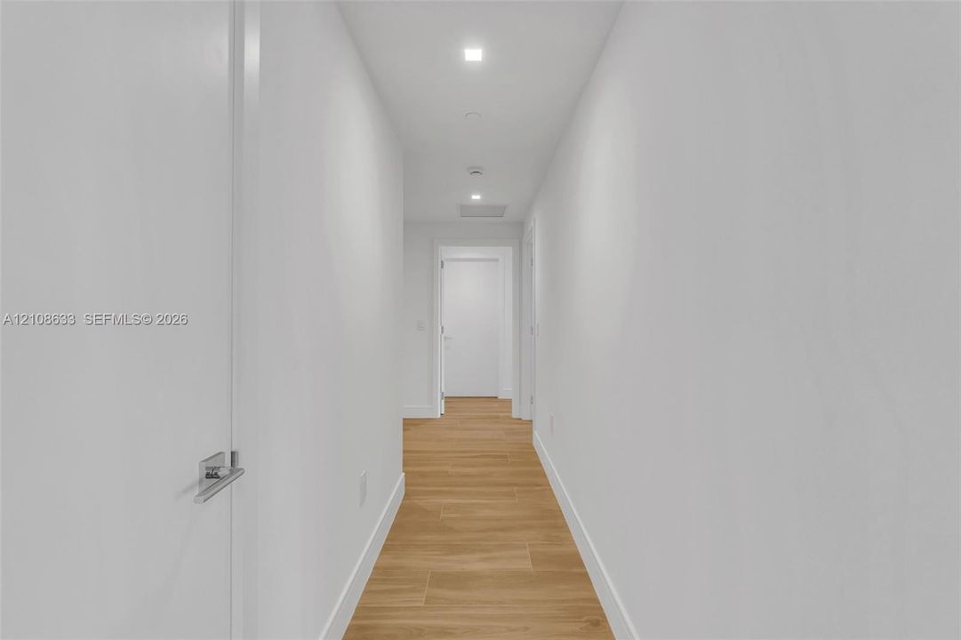 Hallway featuring wood-finish flooring, recessed lighting, and interior doors with brushed metal lever hardware