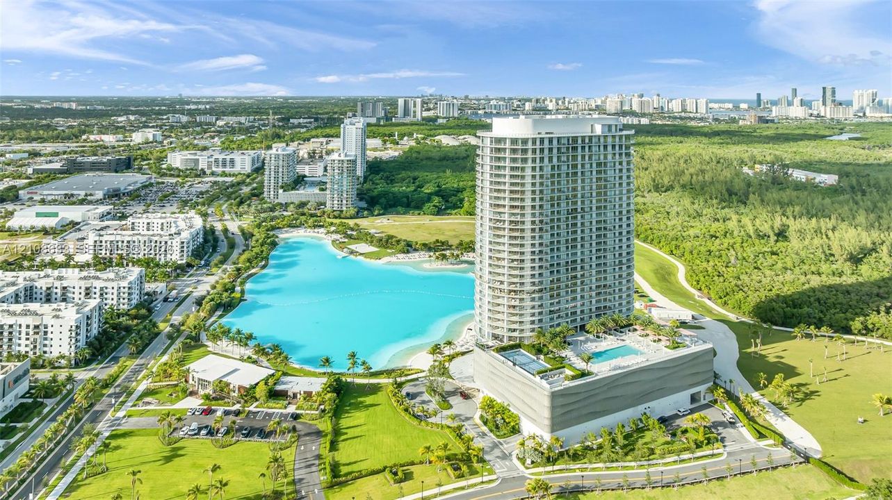 High-rise residential tower featuring a podium-level swimming pool, expansive landscaped grounds, and proximity to a large lagoon