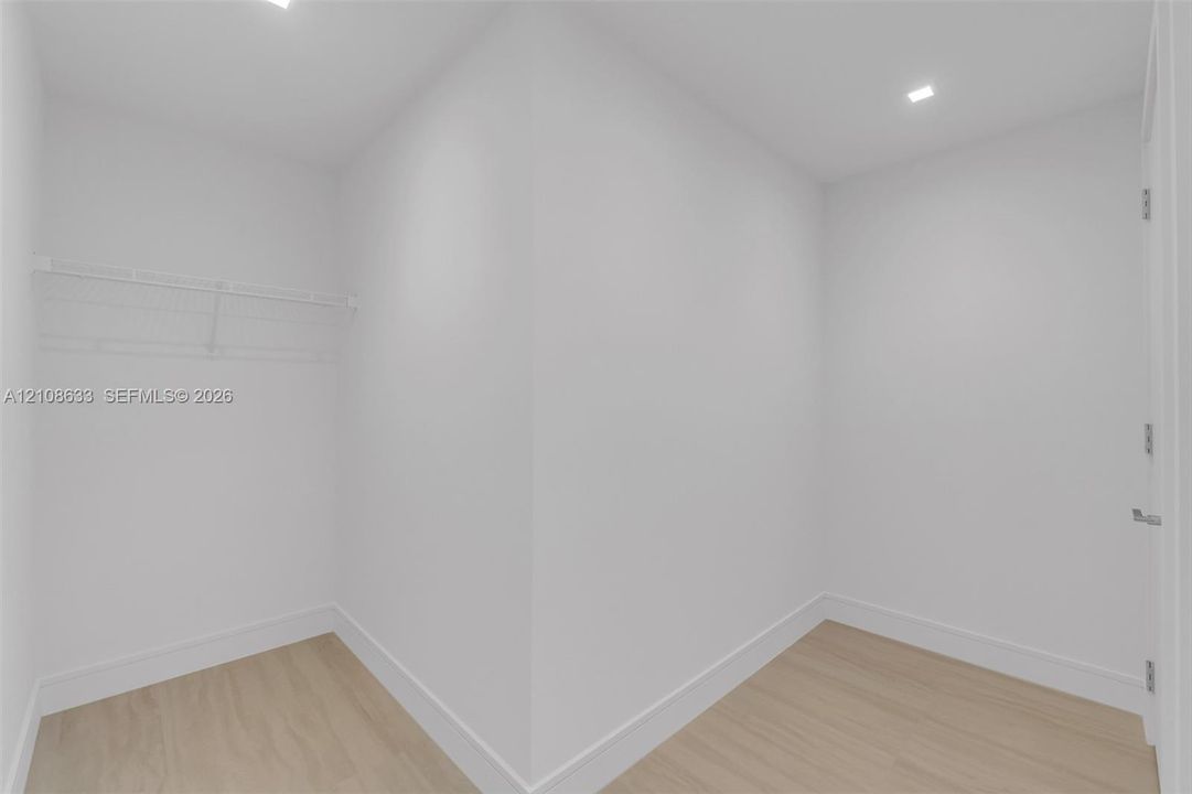 Walk-in storage space featuring wood-finish flooring, white walls, recessed ceiling lighting, and wire shelving