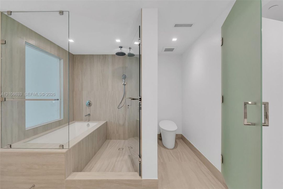 Bathroom featuring wood-finish tile wall and floor surfaces, a soaking tub with a glass partition, a walk-in shower with a dual-head fixture, and a frosted glass door entry