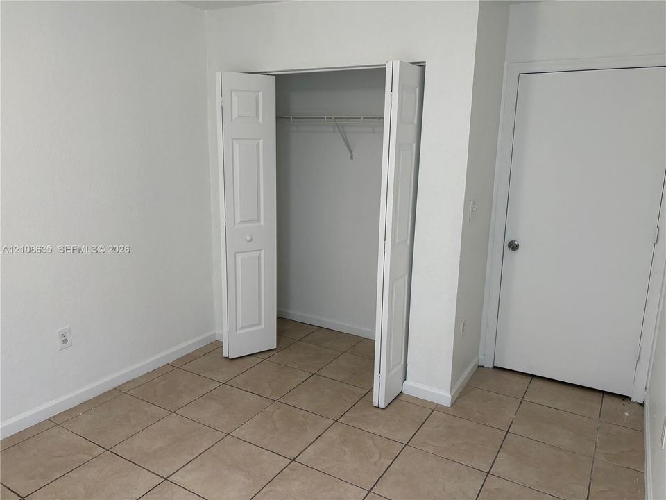 Room featuring neutral-toned tile flooring, white walls, a bifold closet door, and a paneled interior door