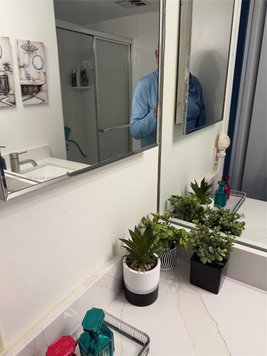 Bathroom vanity featuring a solid-surface countertop with an integrated rectangular sink and a single-handle chrome faucet, complemented by a large wall-mounted mirror and a glass-enclosed shower