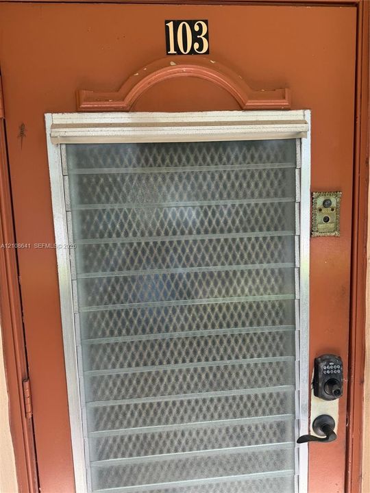 Solid entry door with a decorative arched transom, integrated metal security screen, push-button electronic keypad lock, and antique-style metal doorbell fixture