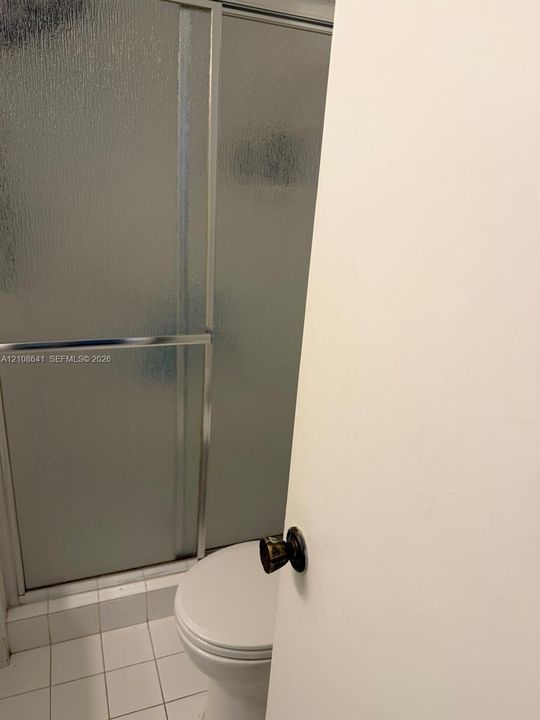 Shower enclosure featuring textured glass panels with a chrome frame, white floor tiling, and a standard toilet