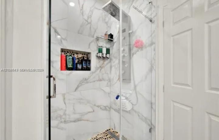 Walk-in shower featuring large-format wall tile, glass enclosure, built-in recessed storage niche, multi-head shower panel system, and pebble-finish flooring