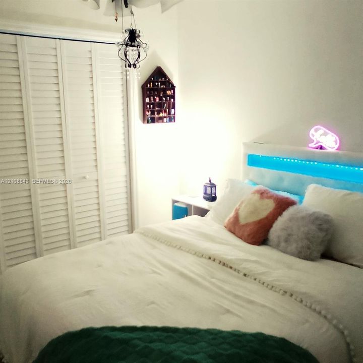 Bi-fold louvered closet doors, decorative hanging ceiling light fixture, and built-in wall-mounted shelving unit