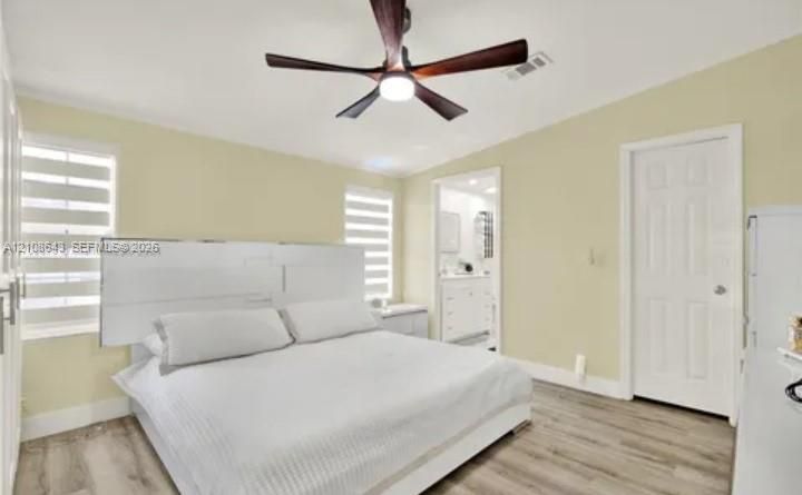 Room featuring wood-finish flooring, a multi-blade ceiling fan with integrated lighting, and dual windows with fitted light-filtering shades