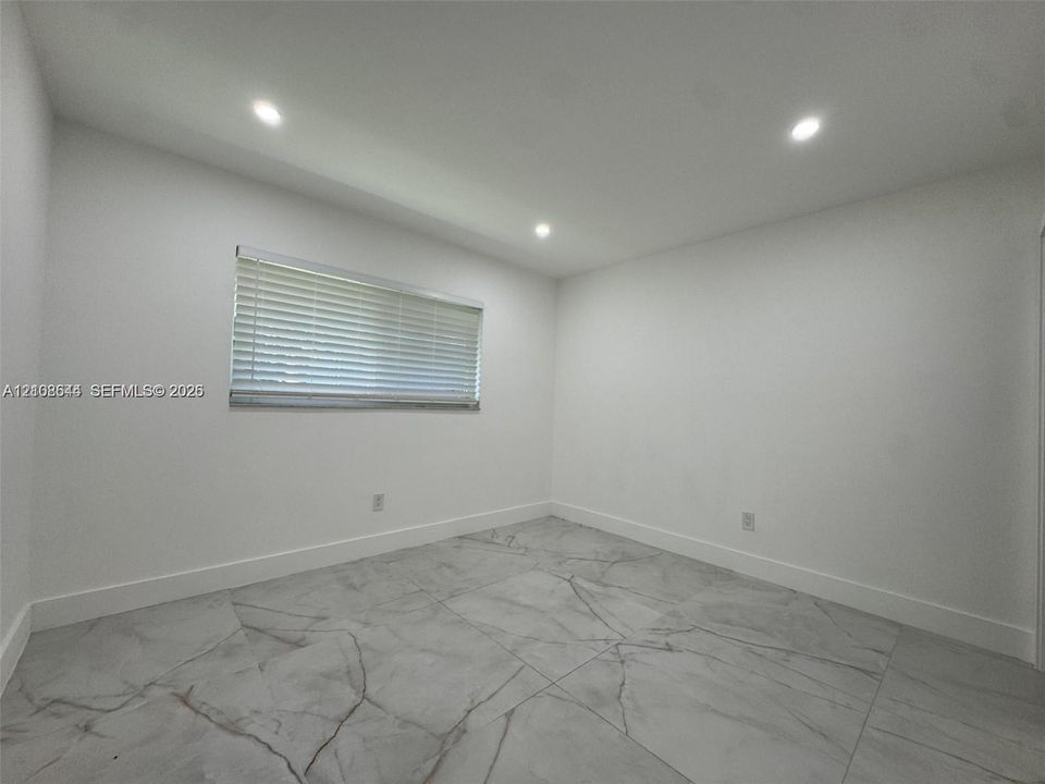 Interior room featuring large-format veined tile flooring, recessed ceiling lighting, and a single window with horizontal blinds