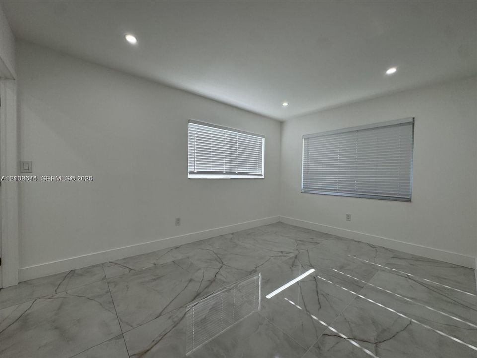 Room featuring large-format tile flooring with a veined pattern, recessed ceiling lighting, and two windows equipped with horizontal blinds