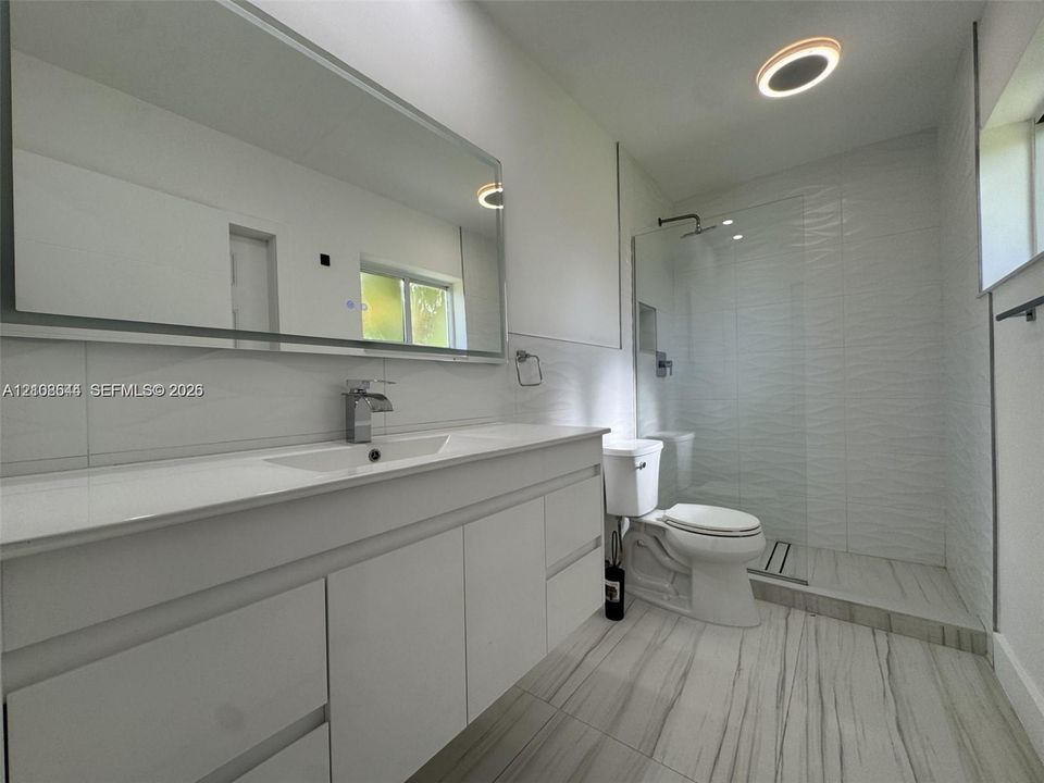 Bathroom featuring a large-format white vanity with a rectangular sink, oversized wall-mounted mirror, walk-in glass shower enclosure with textured tile walls, and large-format tile flooring