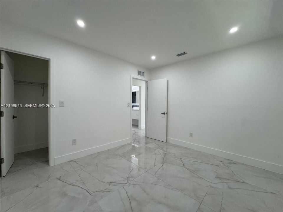 Large-format polished tile flooring with veining detail, recessed ceiling lighting, and built-in closet storage
