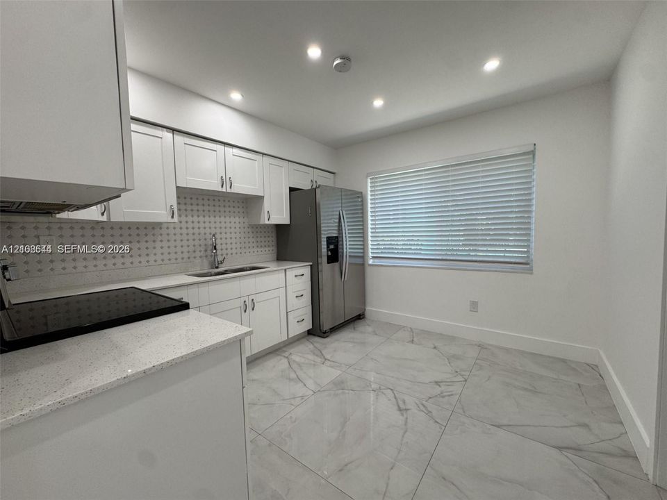 Kitchen featuring white cabinetry, quartz countertops, a patterned tile backsplash, large-format polished tile flooring, and stainless steel refrigerator