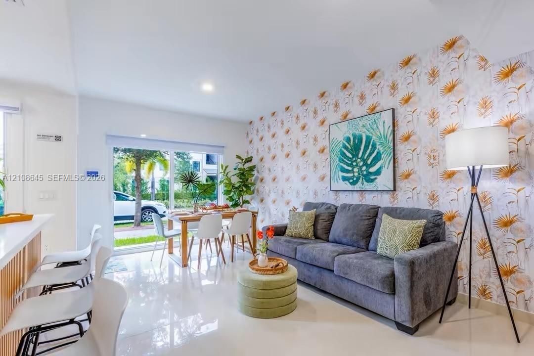 Open living area featuring large-format tile flooring, a statement patterned accent wall, and sliding glass doors providing access to the outdoors