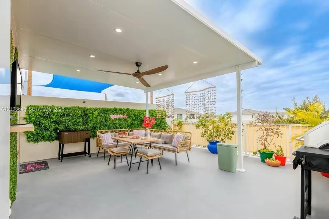Covered outdoor rooftop patio featuring a smooth concrete surface, recessed ceiling lighting, a dark wood-finish ceiling fan, and a green wall installation