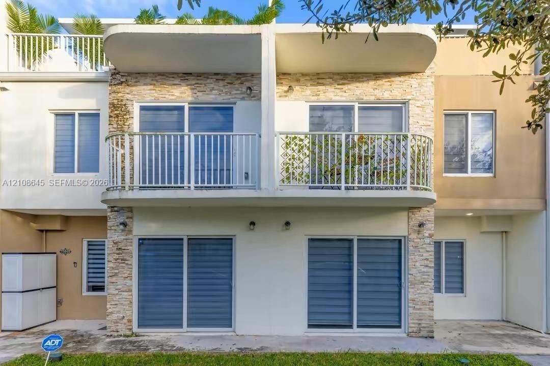 Multi-level exterior featuring stacked stone veneer, private upper-level balcony with metal railings, and dual-level sliding glass doors