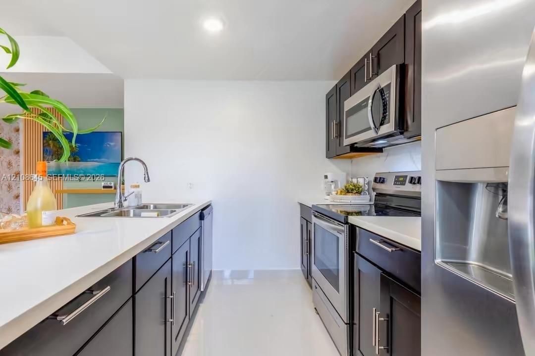 Kitchen featuring dark cabinetry, solid-surface countertops, dual-basin stainless steel sink with pull-down faucet, and stainless steel appliances