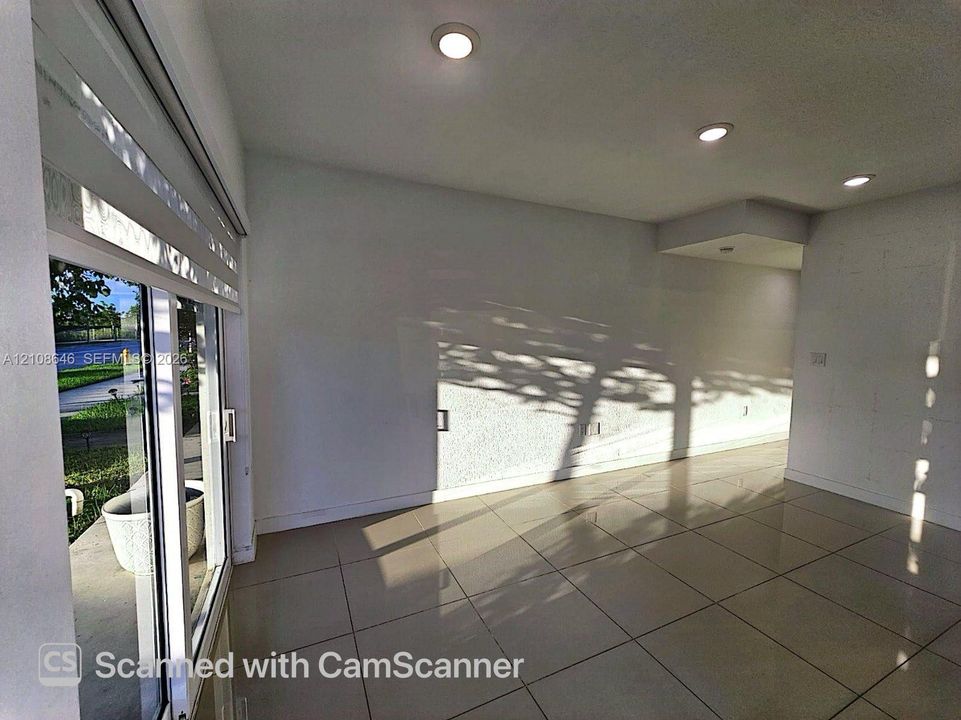 Interior space featuring neutral large-format tile flooring, recessed ceiling lighting, and sliding glass door with roller shade