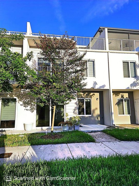 Multi-level exterior featuring white stucco siding, a rooftop terrace with metal railing, sliding glass doors, and concrete walkways