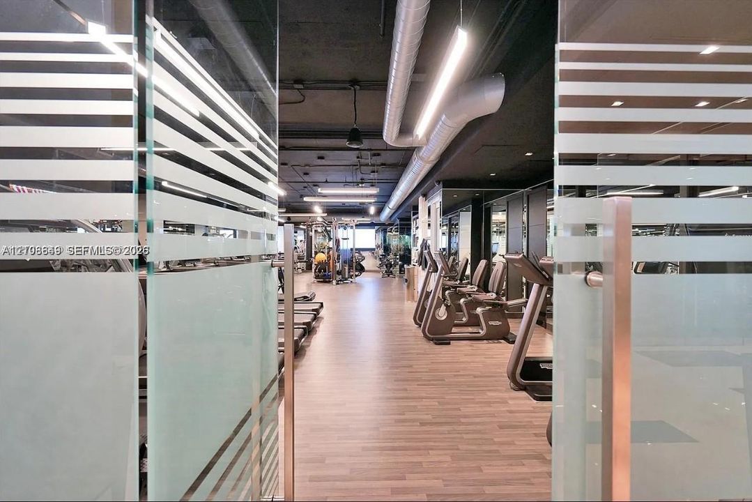 Glass doors with frosted horizontal detailing, wood-finish flooring, exposed industrial-style ceiling with ductwork, and linear overhead lighting