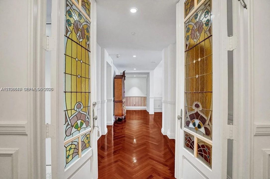 Double doors featuring decorative stained-glass panels, wood-finish flooring laid in a herringbone pattern, wainscoting, and recessed ceiling lighting