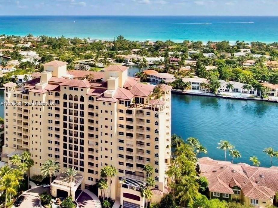 High-rise building with a multi-level concrete facade, tile roofline, numerous exterior balconies, and a porte-cochere entry, situated on a waterfront lot with canal access