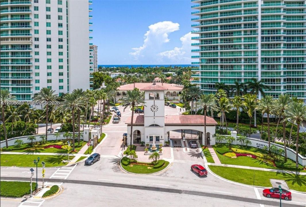 Gated entrance featuring a clock tower, terracotta-tiled roofs, manicured landscaping, and palm-lined grounds