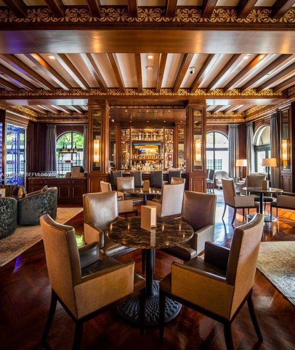 Ornate wood-paneled lounge featuring an intricate coffered ceiling with gold-leaf detailing, polished wood-finish flooring, built-in bar cabinetry, and arched windows