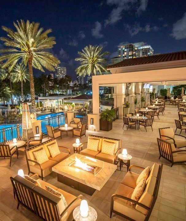 Expansive outdoor terrace featuring stone flooring, a built-in fire pit with a stone surround, and an integrated swimming pool with metal safety railing