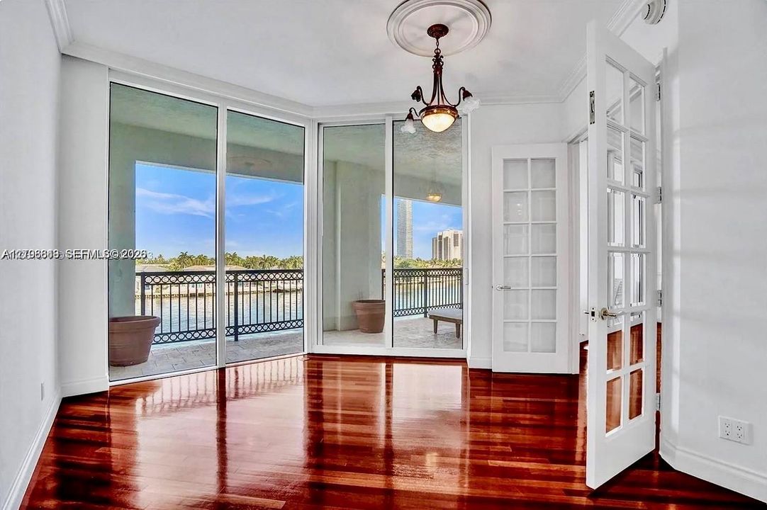 Room featuring polished wood-finish flooring, floor-to-ceiling glass paneling, a decorative ceiling medallion with an attached chandelier, and French-style interior doors