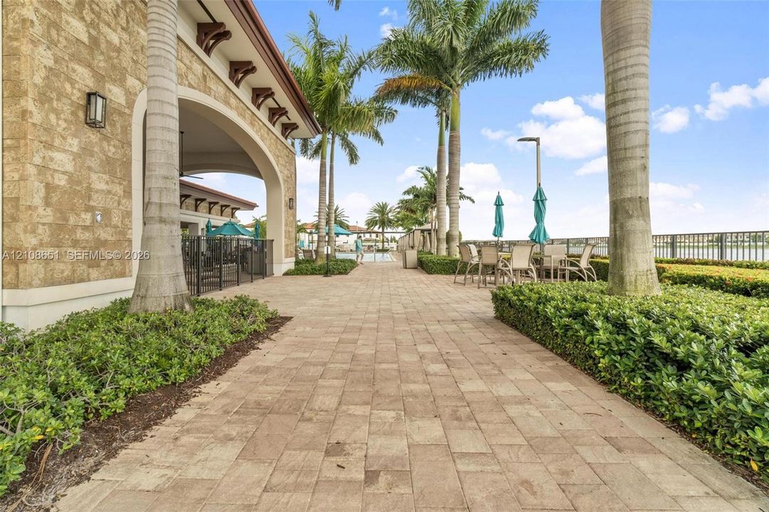 Paver stone walkway featuring a masonry exterior, covered loggia, and landscaped perimeter with mature palm trees