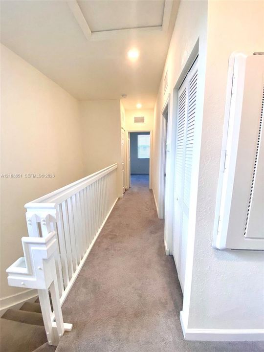 Hallway featuring neutral carpeting, a white-painted wooden balustrade, and louvered bifold closet doors