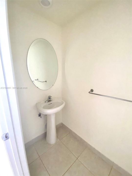 White pedestal sink with chrome faucet, oval wall-mounted mirror, and neutral-toned tile flooring