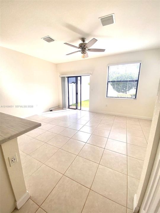 Open floor plan featuring large-format ceramic tile flooring, a central ceiling fan, sliding glass doors, and a single-pane window