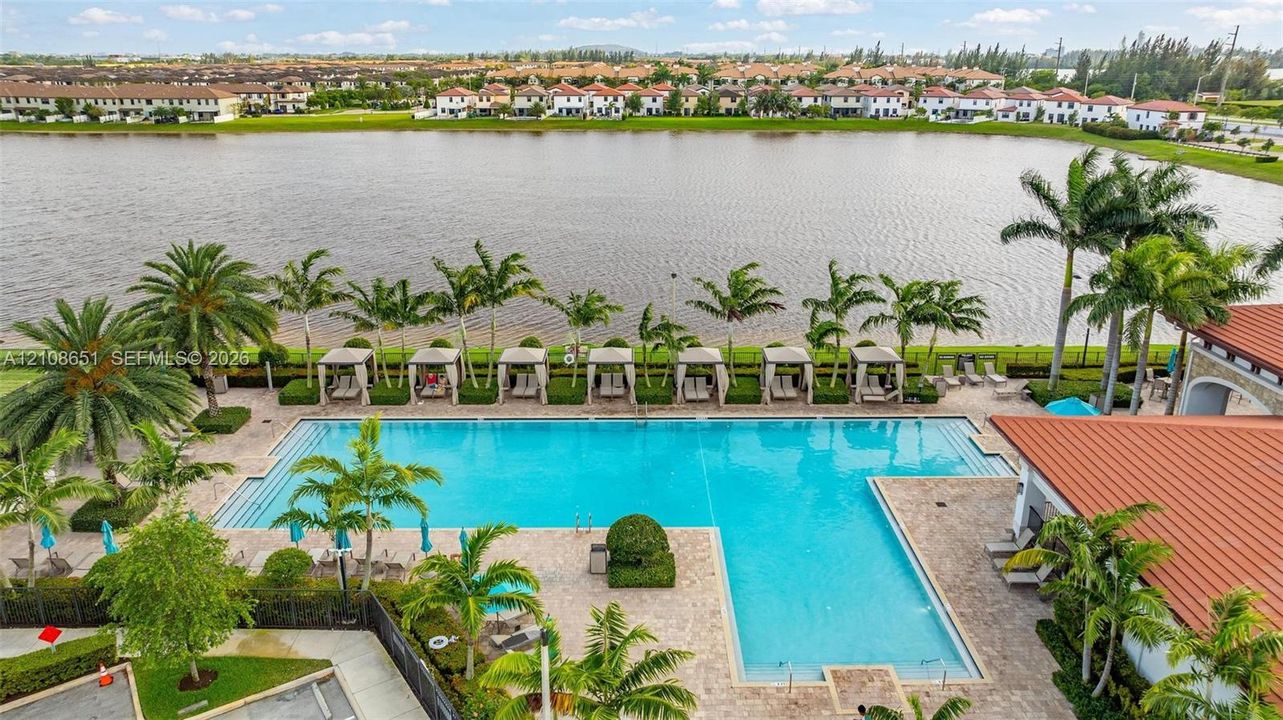 Large swimming pool with paver decking, cabanas, and integrated landscaping overlooking a lake
