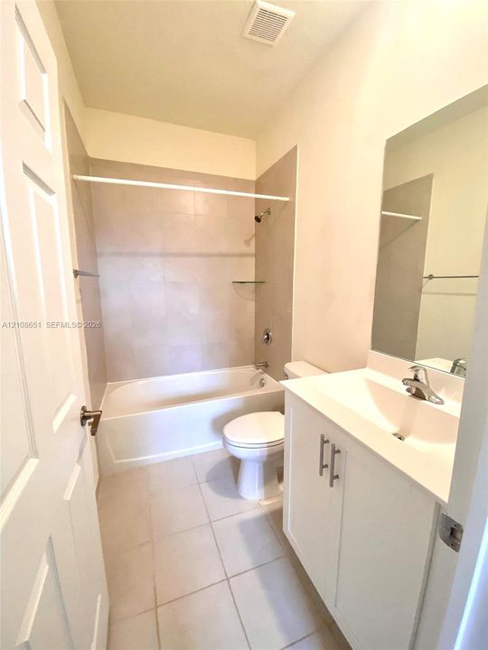 Bathroom featuring a vanity with white cabinetry and a molded sink, large wall-mounted mirror, tub-shower combination with light-toned tile surround, and neutral floor tile