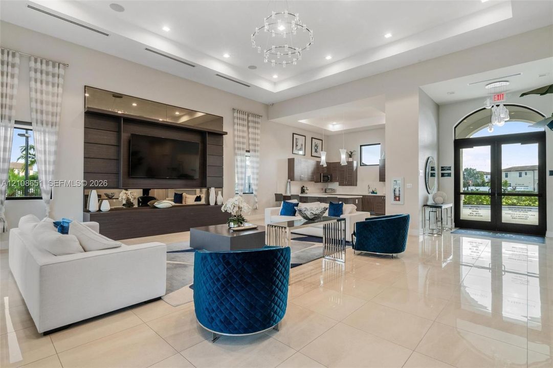 Tray ceiling with integrated recessed lighting, polished large-format tile flooring, built-in media center with dark wood cabinetry, chandelier light fixtures, and glass-paned double entry doors with arched transom