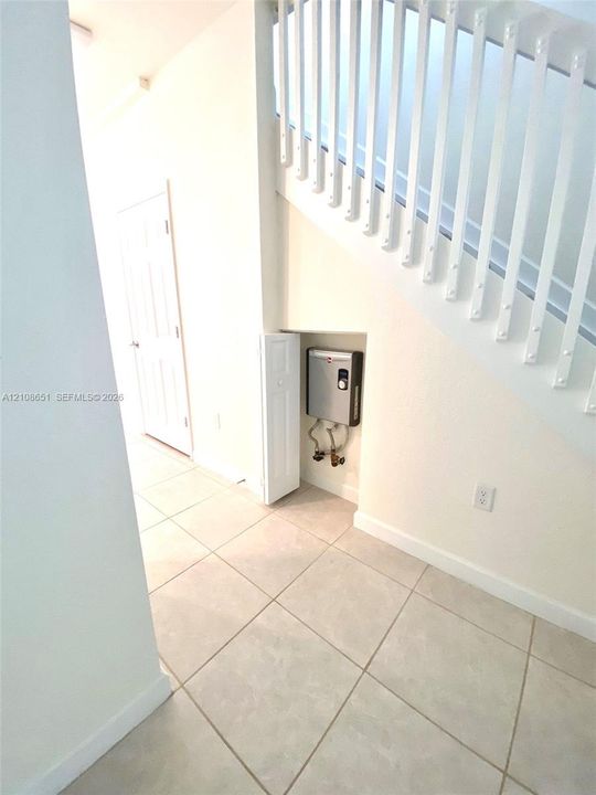 Staircase featuring white balusters and a handrail, ceramic tile flooring, and a recessed storage area housing a tankless water heater