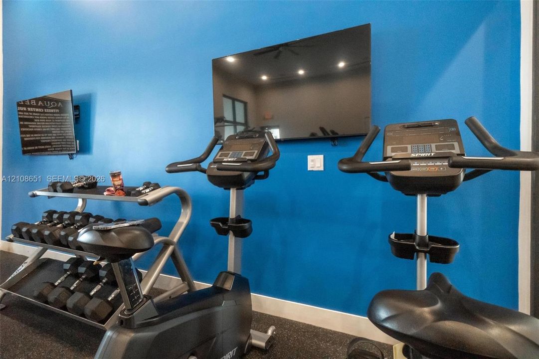 Fitness center featuring wall-mounted television, rubberized flooring, and recessed ceiling lighting